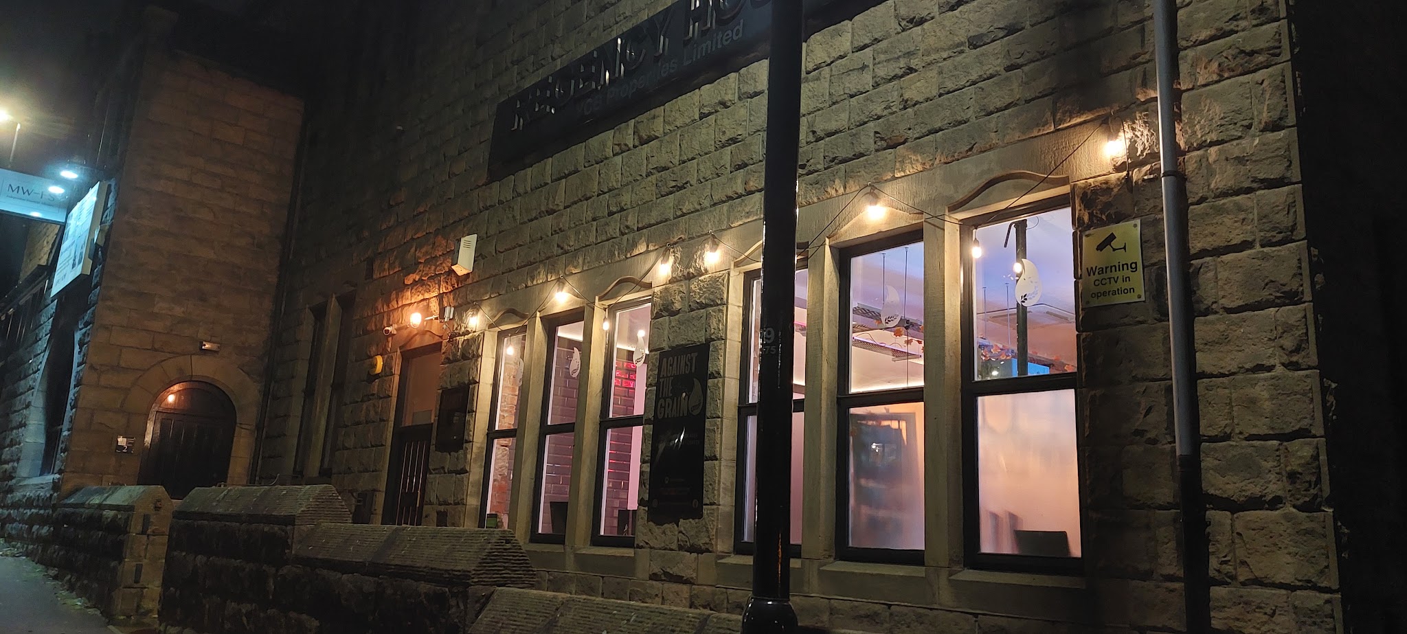 Warmly lit Against The Grain bar behind its stone frontage on Kirk Lane